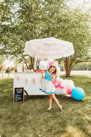 Outdoor party setup with white parasols, balloons, and cotton candy station on a grassy lawn.