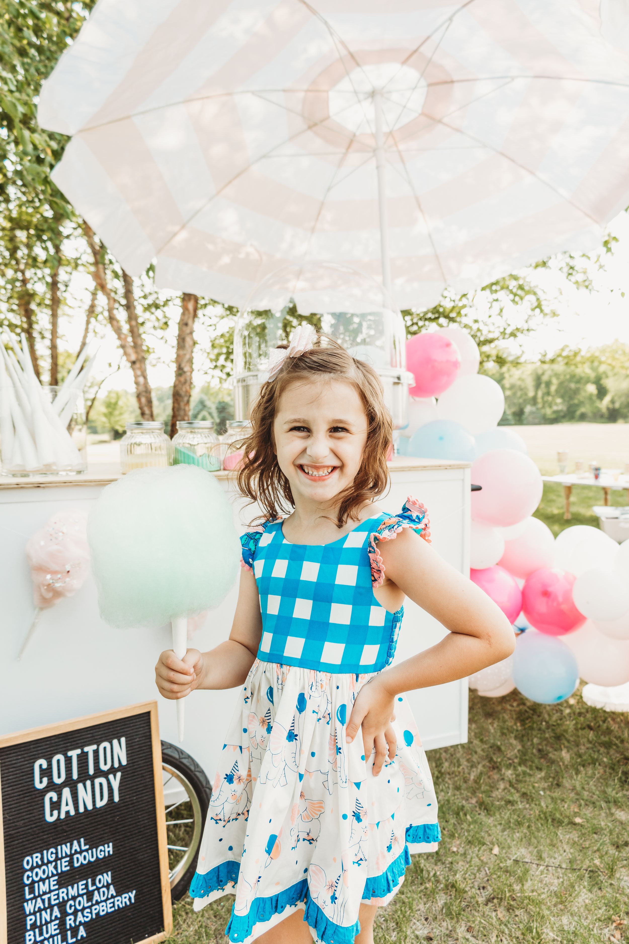 Festive outdoor cotton candy party setup with blue and pink balloons and decorative umbrellas.