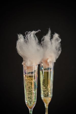 Champagne flutes with cotton candy garnish creating a whimsical effect against dark background.