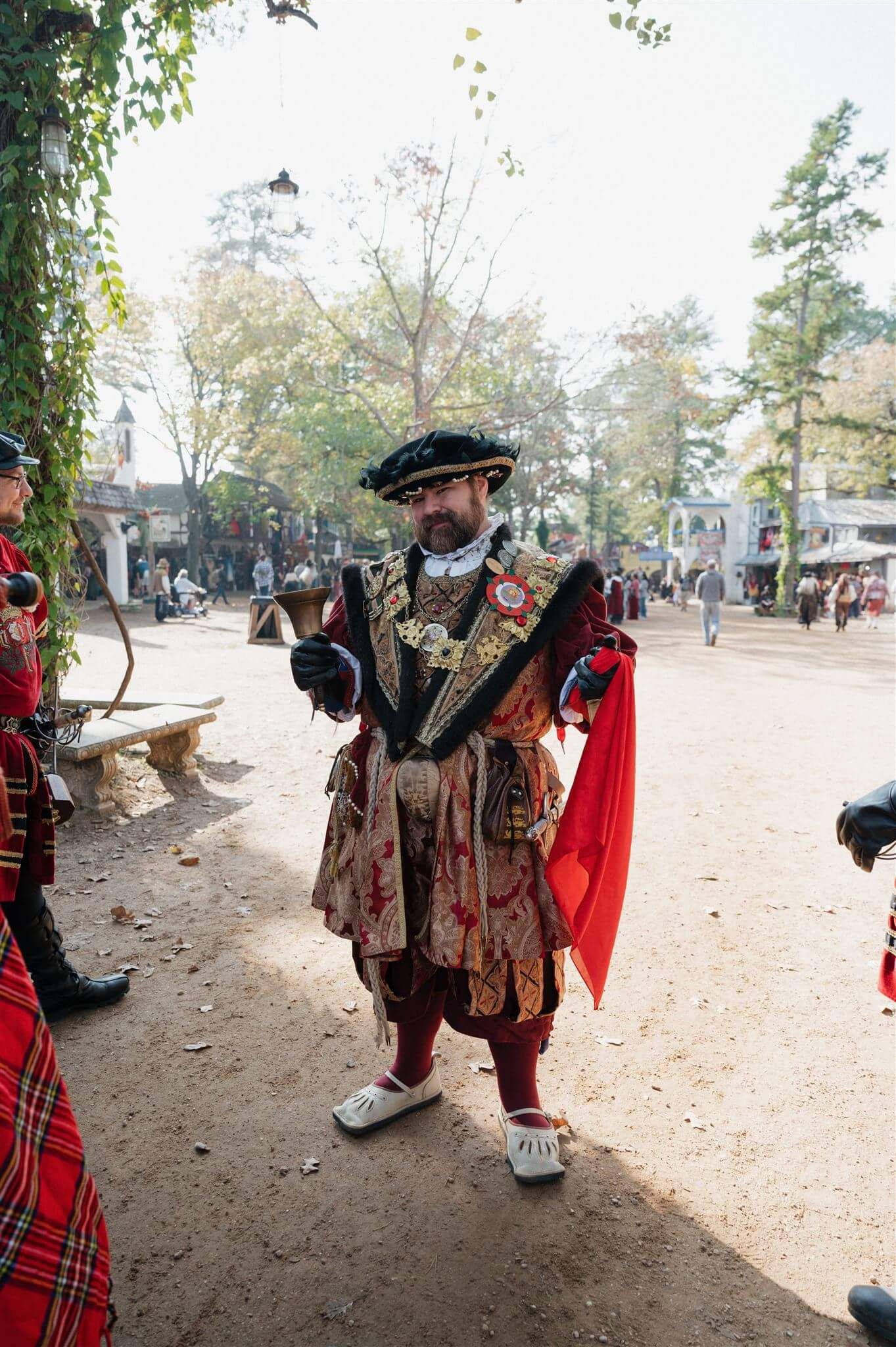 A performer in elaborate Tudor-style costume with ruffled collar gestures at renaissance faire.