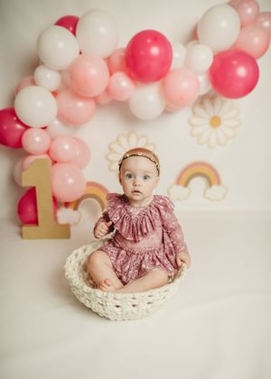 Pink and white balloon arch with rainbow decorations and floral accents for birthday photography.