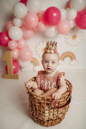 First birthday photo setup with pink balloons, basket prop, and gold number one decoration.