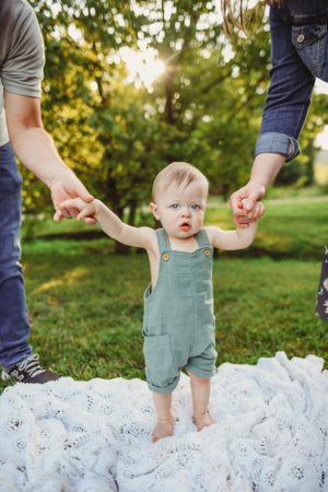 Outdoor photo session on white blanket with green grass and trees in background.