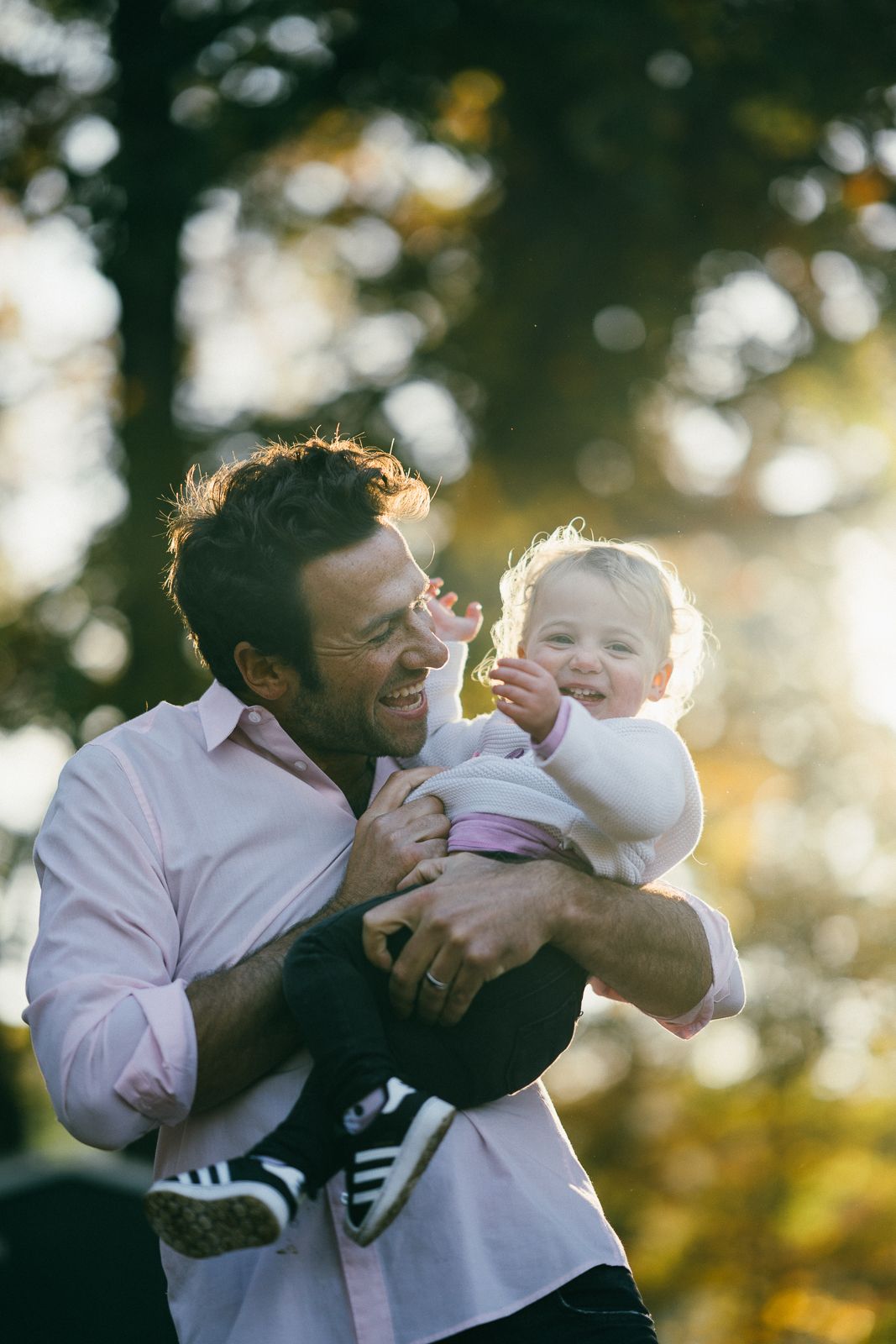 A joyful moment shared between parent and baby backlit by golden sunlight in a park setting.