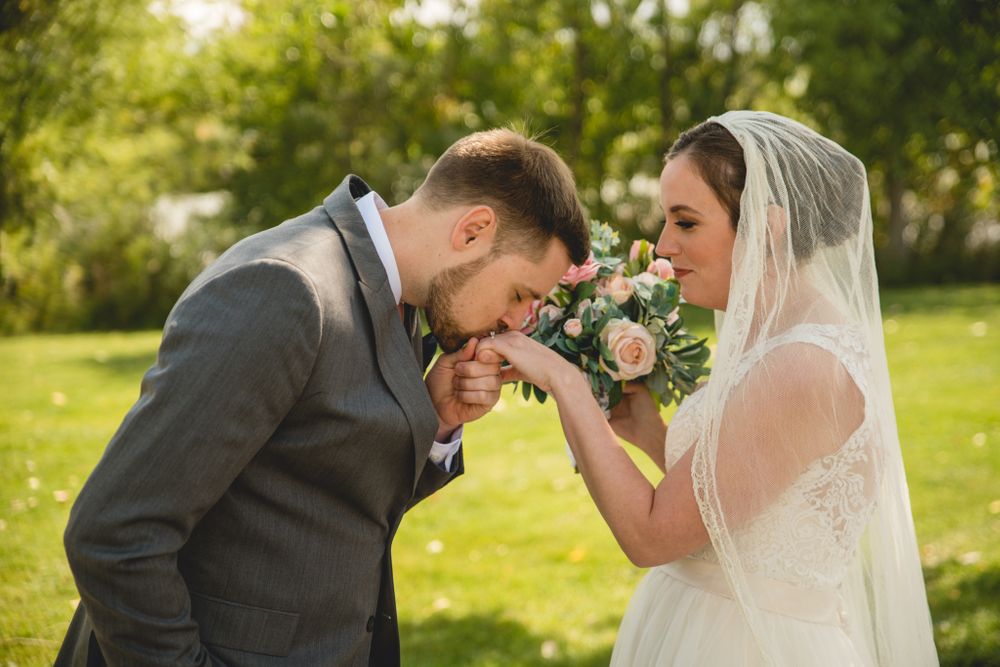 Romantic wedding couple sharing an intimate moment with a floral bouquet in a sunny garden.