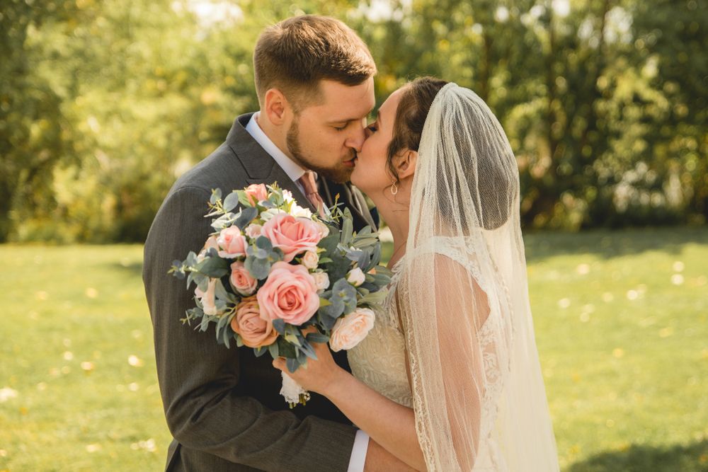An intimate wedding portrait with pink roses and flowing veil in golden afternoon light.