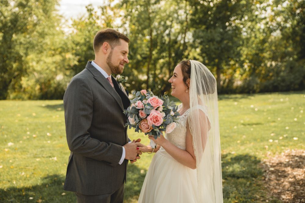 A romantic outdoor wedding moment with a beautiful bouquet of pink roses under sunlit trees.