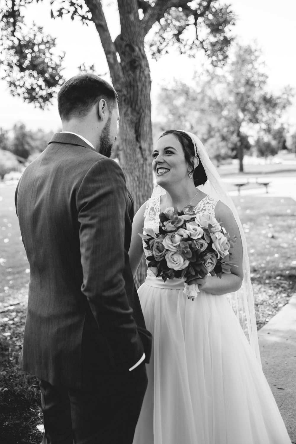 A candid black and white wedding moment captured under a large tree.