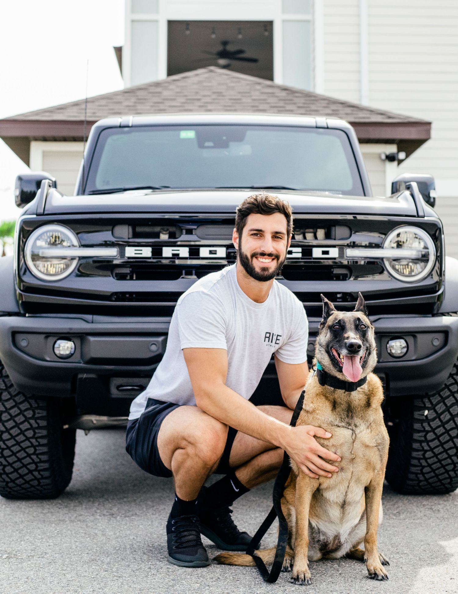 Man and malinois sitting in front of bronco for a photo