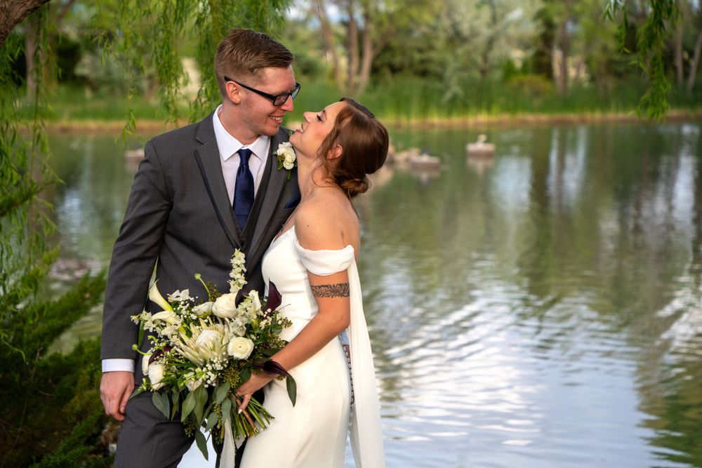 Newlyweds embrace by a lake while holding a white and green bouquet. Wedding Photography Sedona