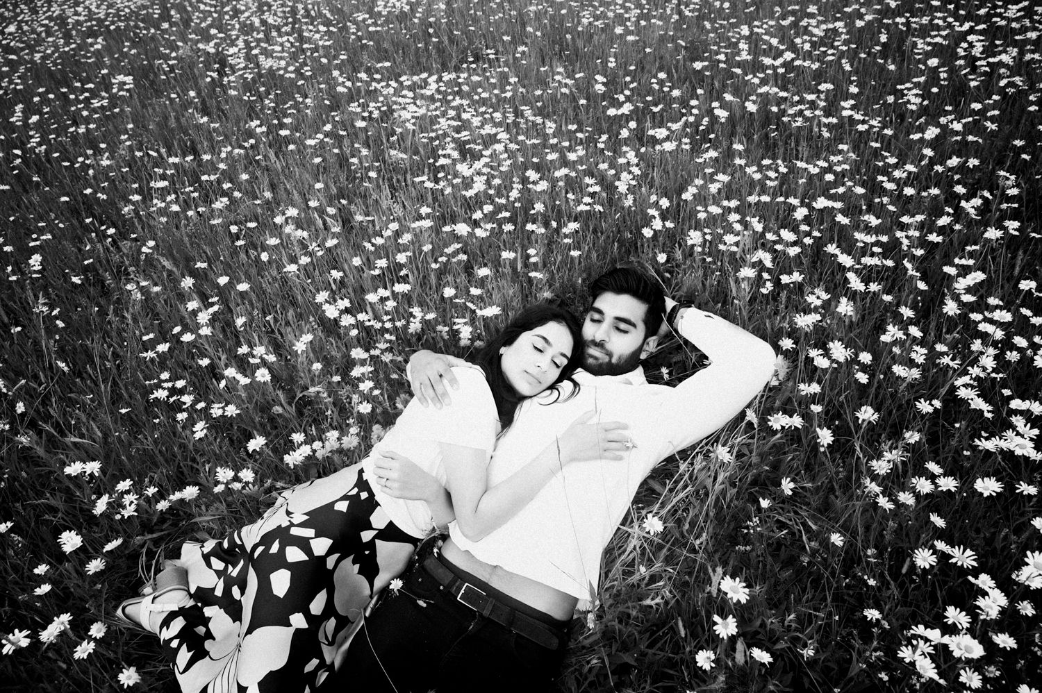 Black and white photo of couple lying in field of flowers creating romantic atmosphere.