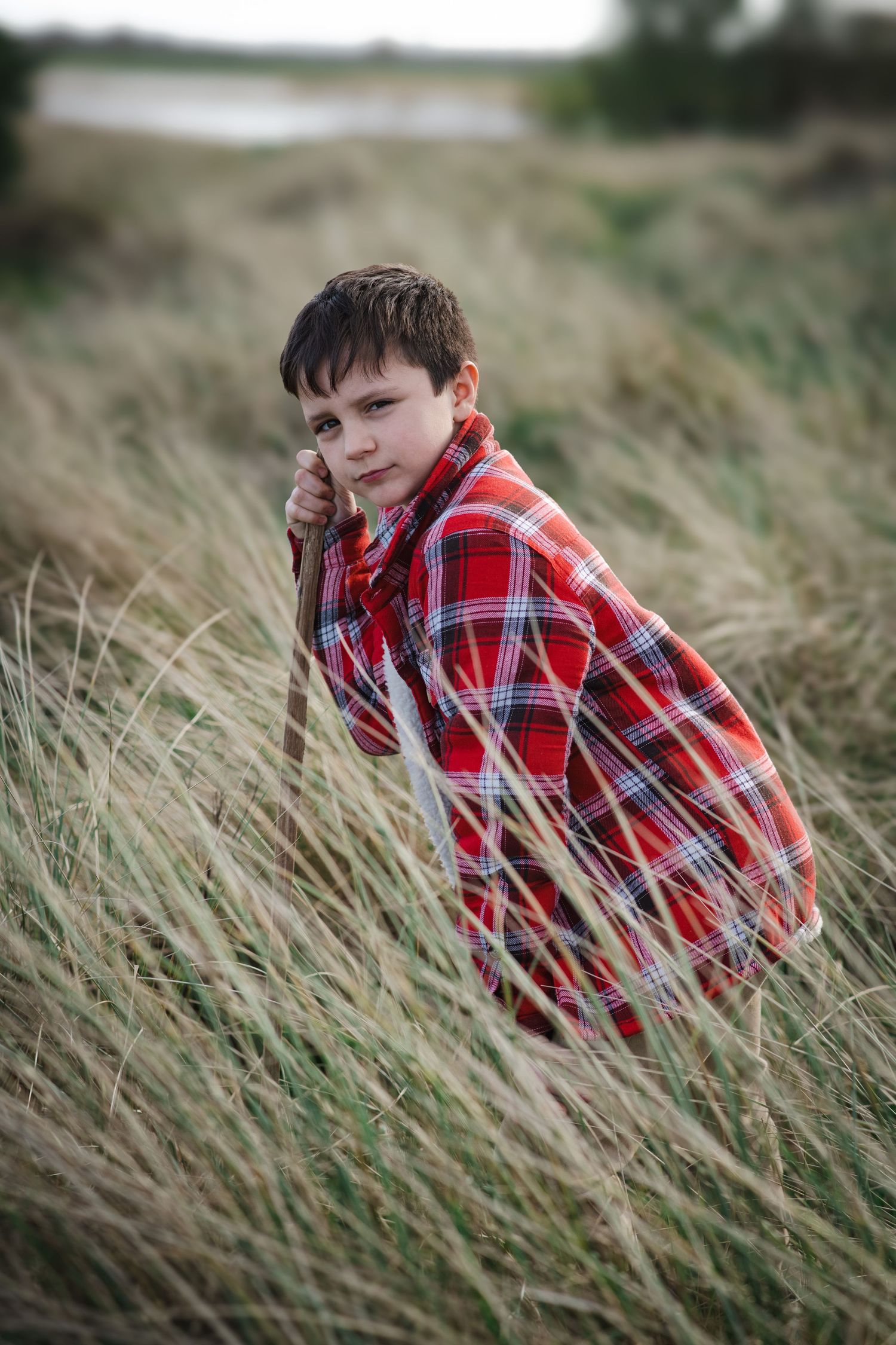 Portrait in red plaid shirt against windswept grass field.