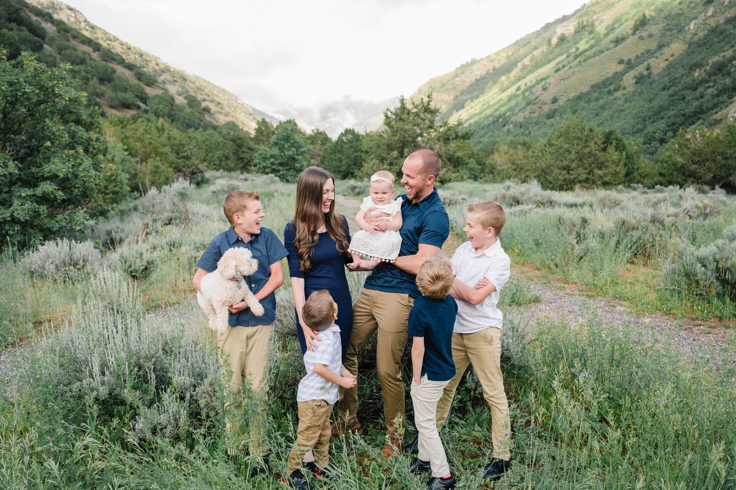 Family group poses together on mountain trail with scenic valley landscape in background.