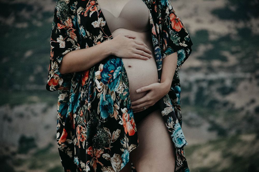 Close-up of pregnant woman in floral kimono holding baby bump outdoors in nature setting.
