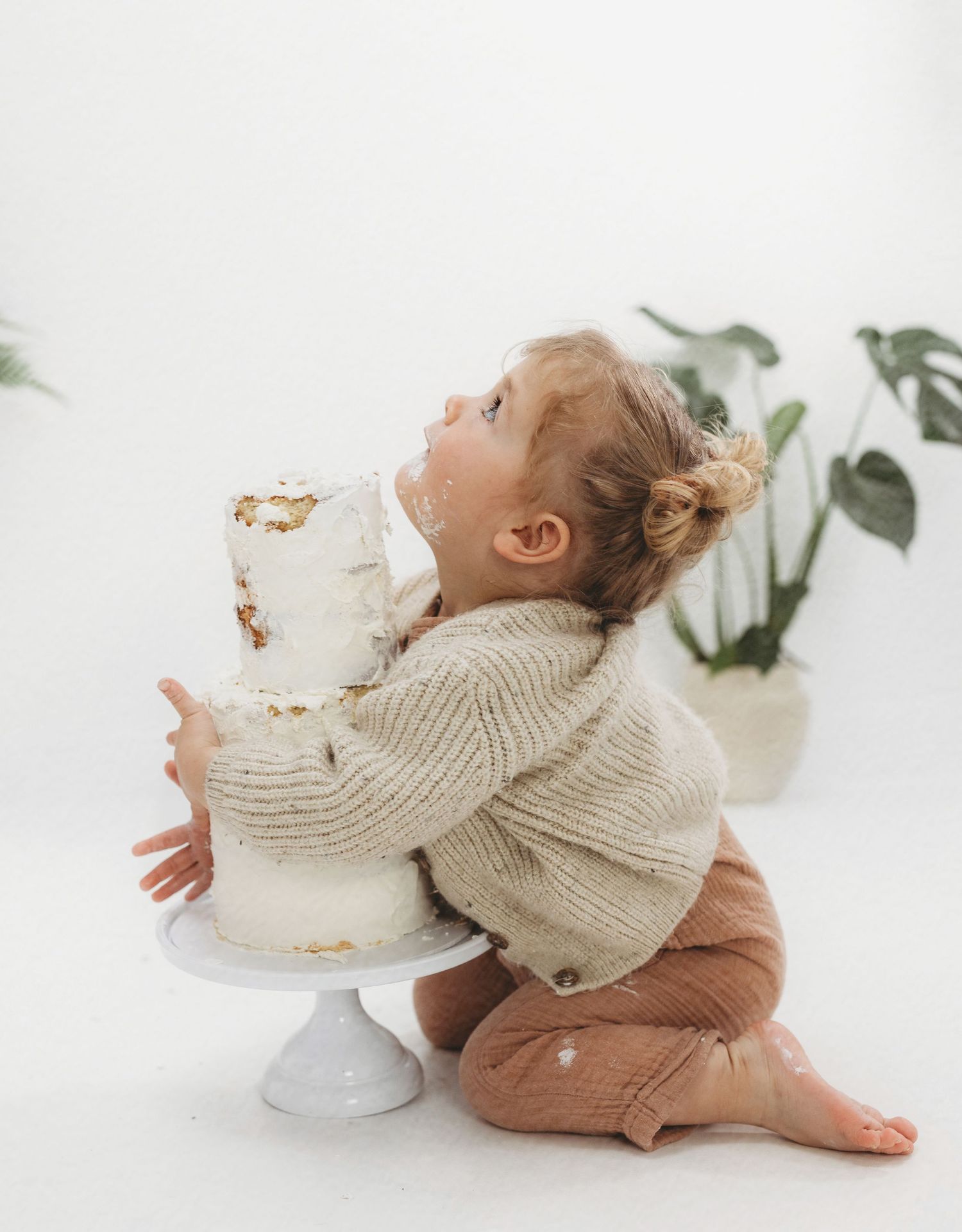 Toddler in knit sweater reaching up to white cake on pedestal.