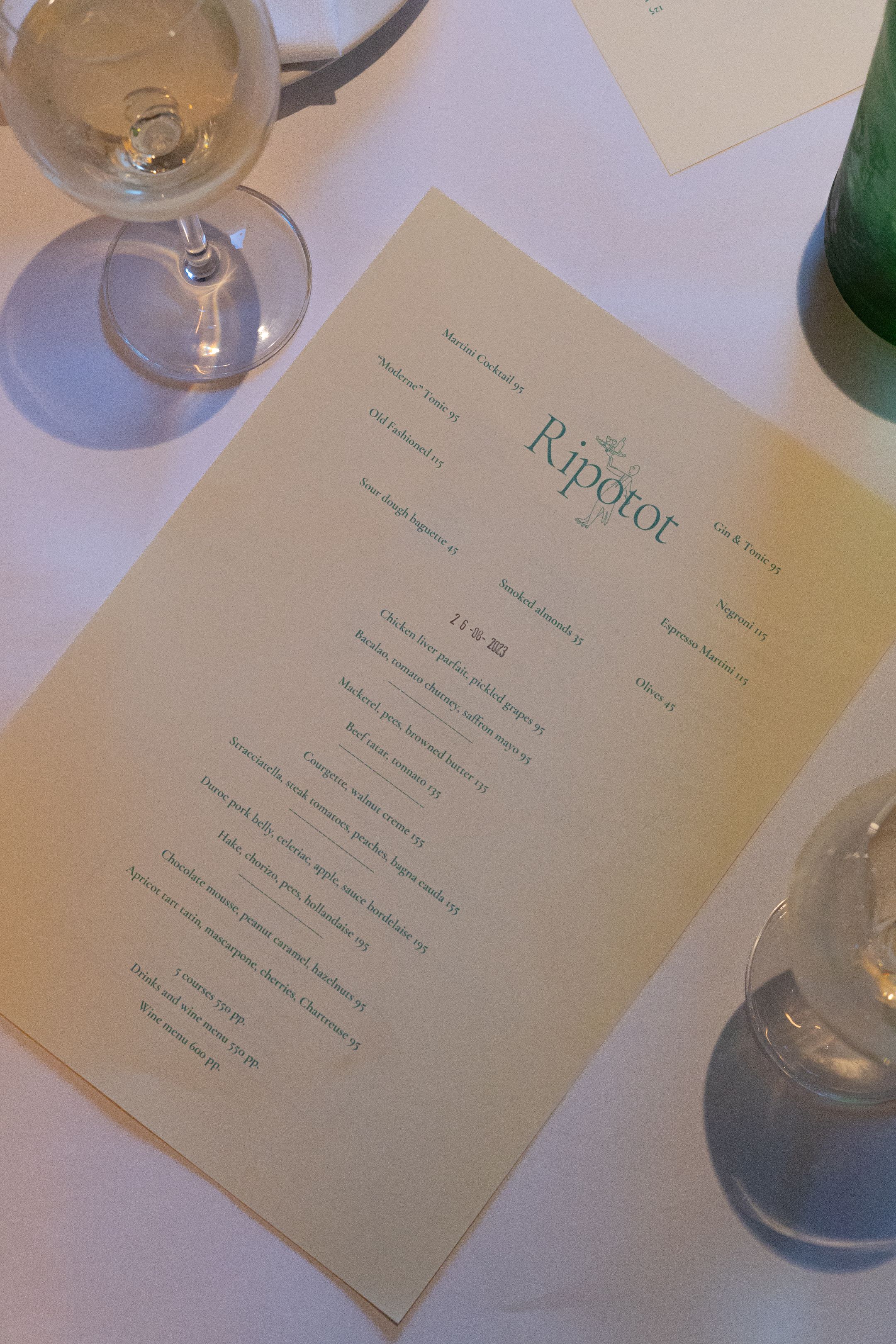 Restaurant menu for 'Kinship' displayed on white tablecloth with wine glasses.