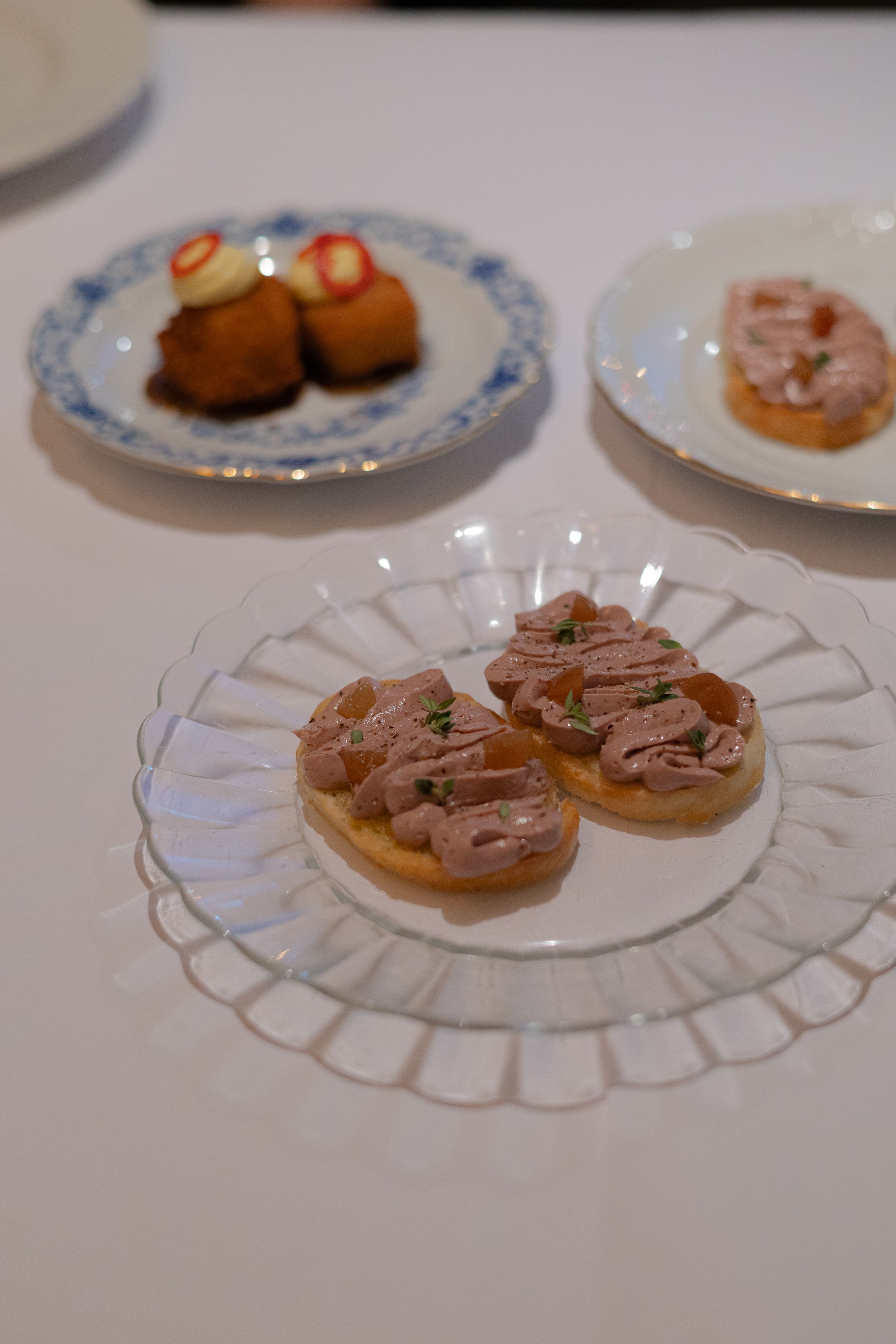 Elegant appetizer plate with small crostini topped with meat on a crystal serving dish.