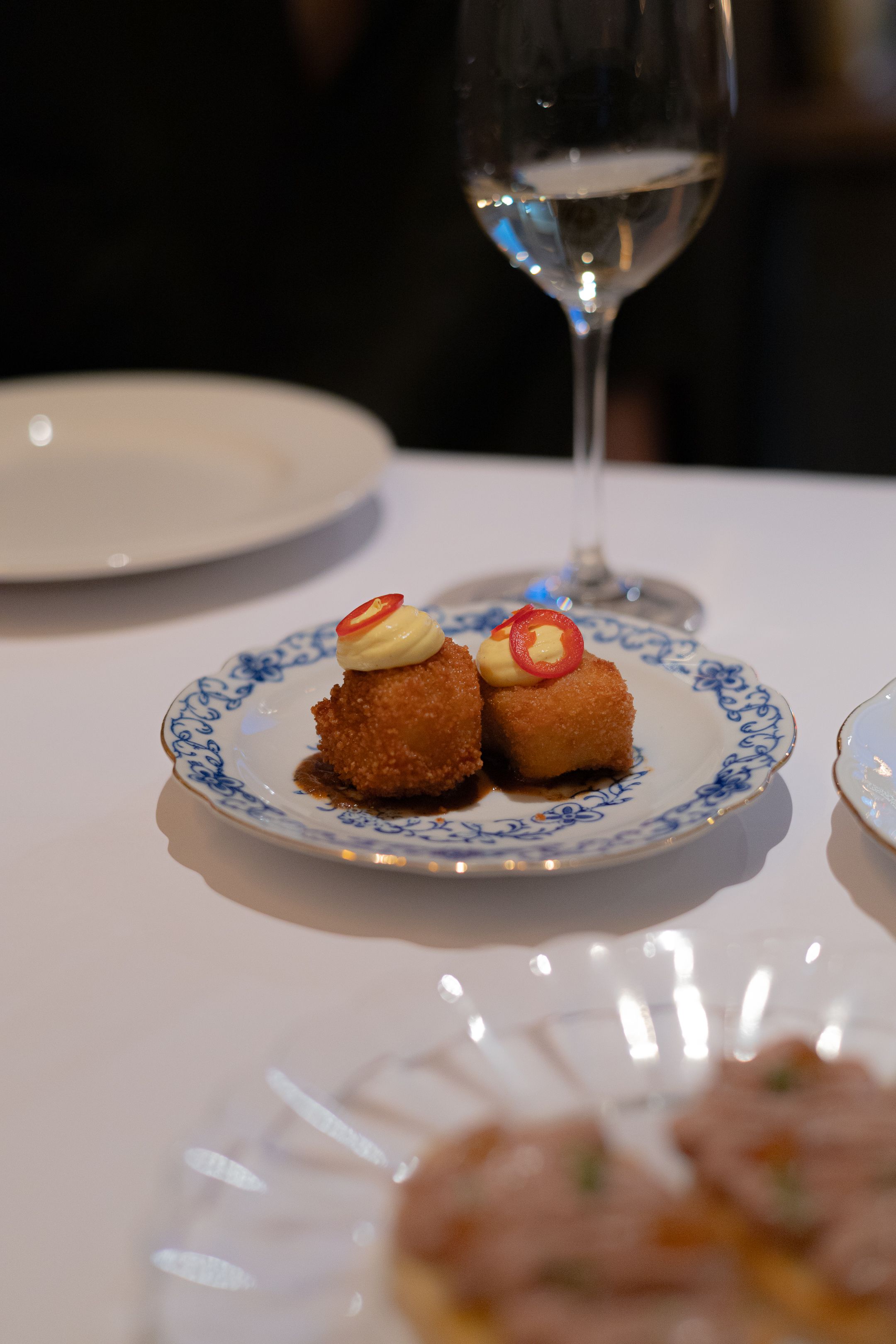 Two golden croquettes garnished with red peppers served on a blue and white china plate.