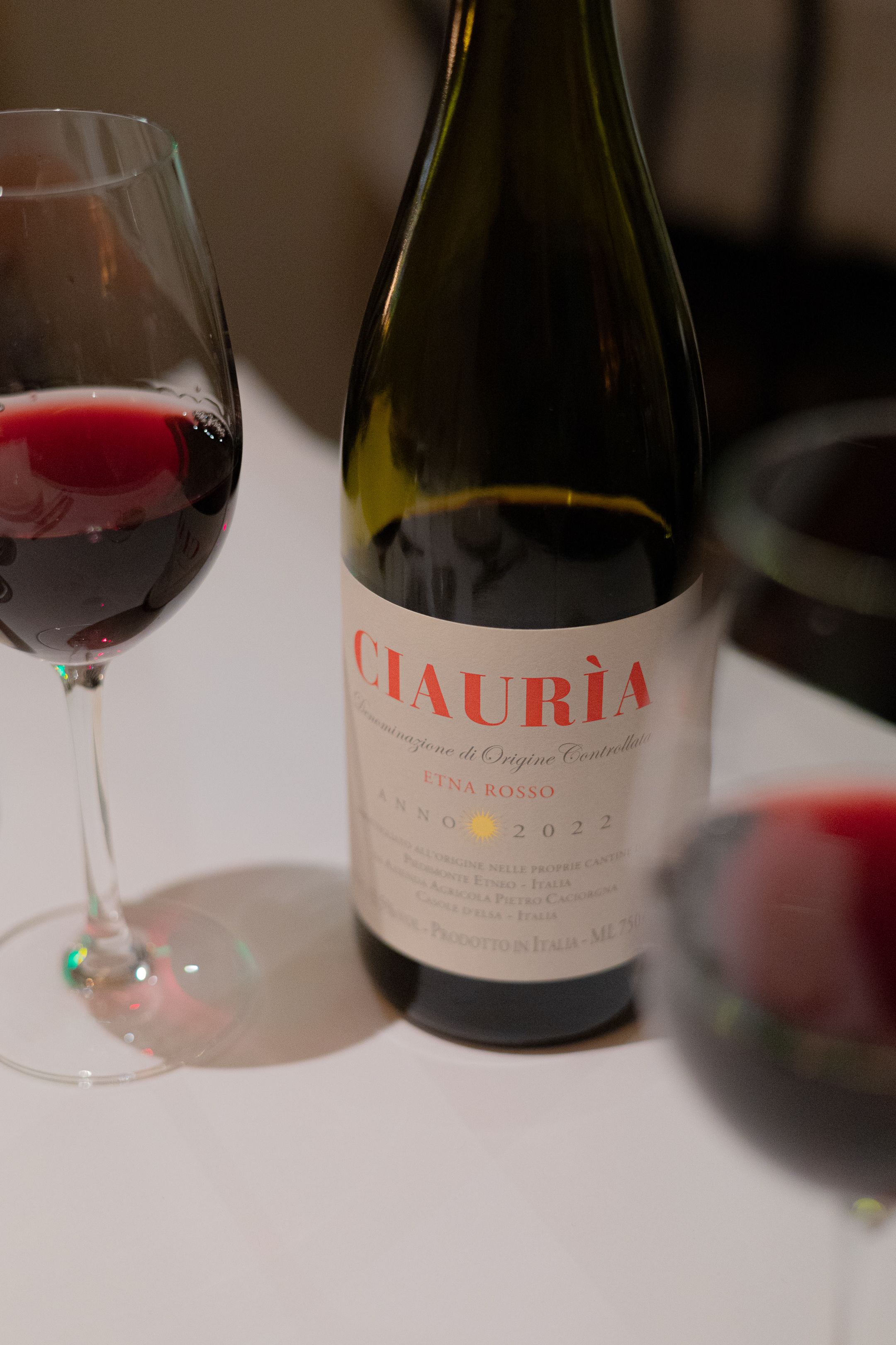 Bottle of Ctauria red wine with filled wine glasses on white tablecloth.