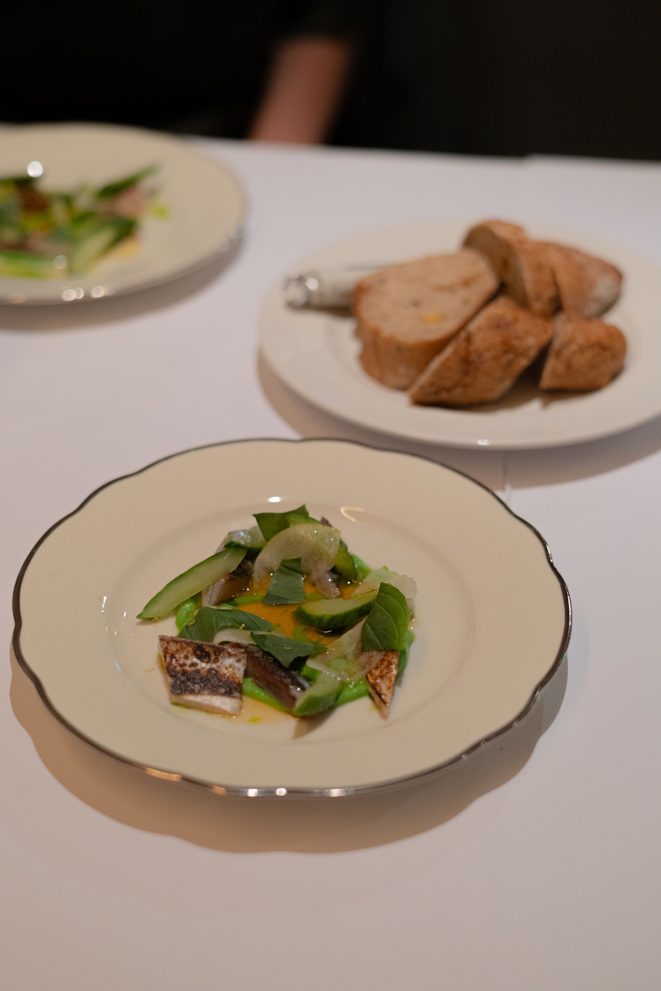 Elegant plated fish dish with fresh greens and crusty bread on white china.