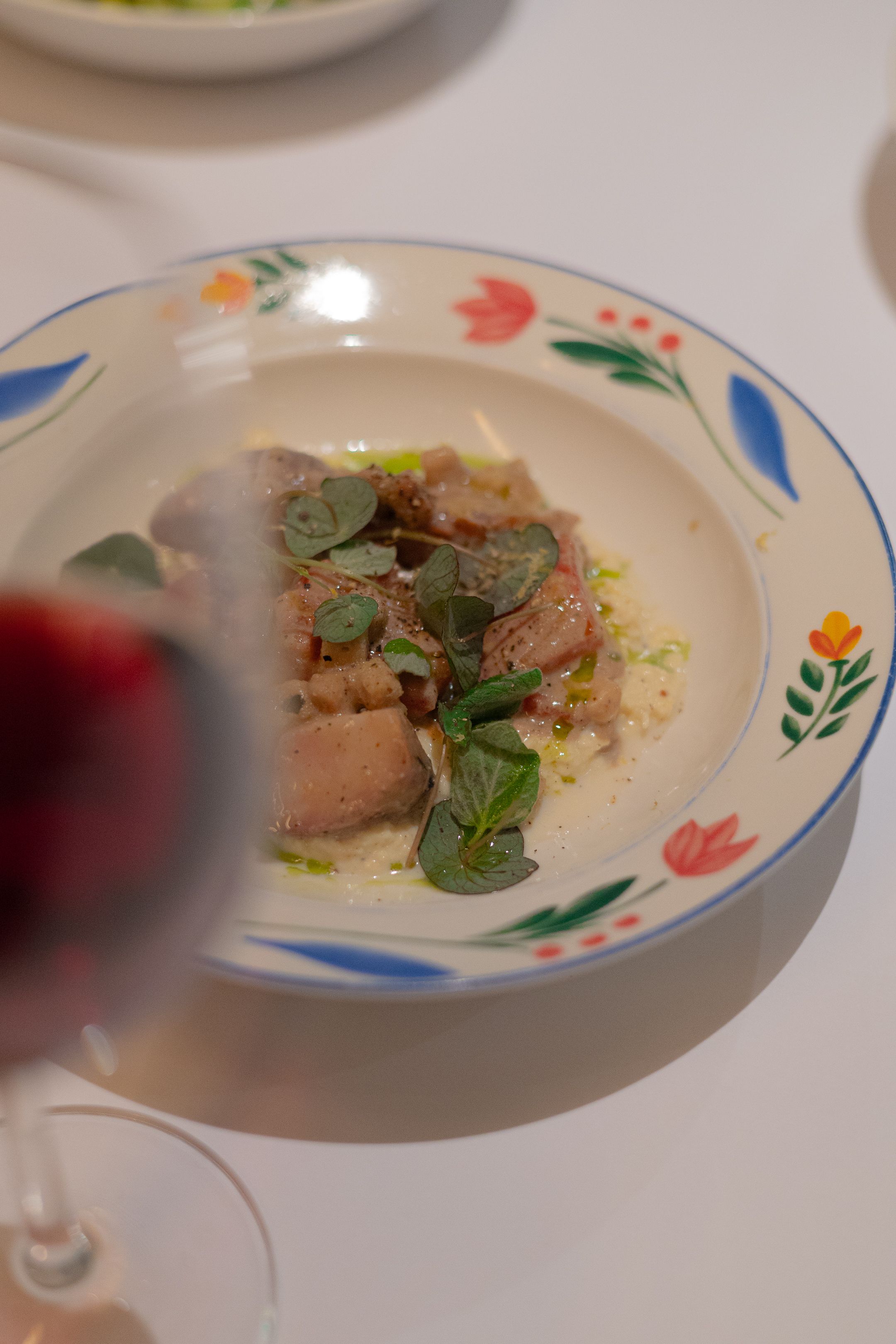 Delicate fish dish garnished with micro greens on a floral patterned plate.