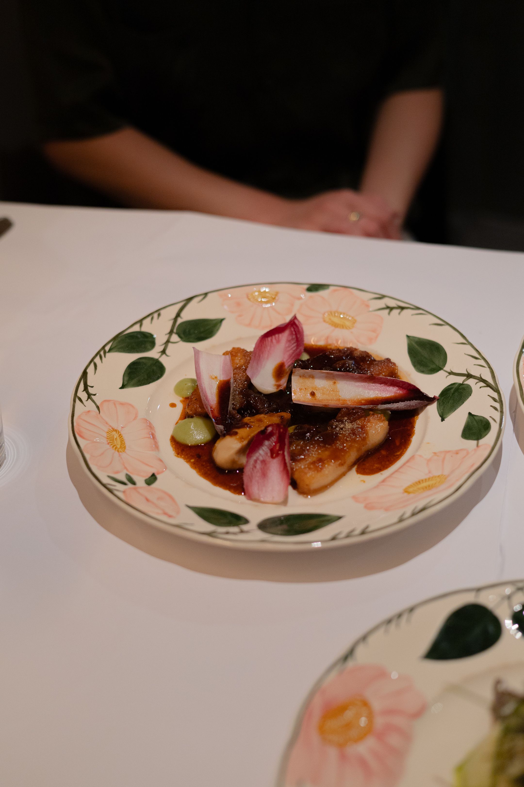 Elegant plated dish with seared meat and red onions on a decorative floral plate.