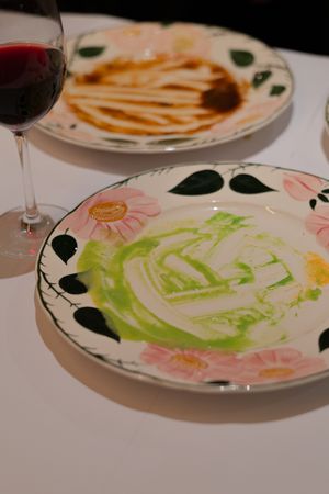 Used dinner plates with artistic green and pink floral patterns and sauce remnants.