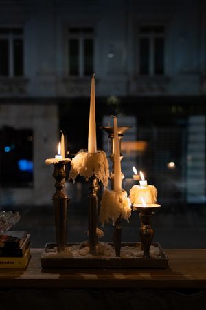 Atmospheric candle display with melting wax drips against dark window backdrop.