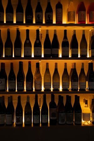 Backlit wine bottle display showing rows of bottles on illuminated wooden shelves.