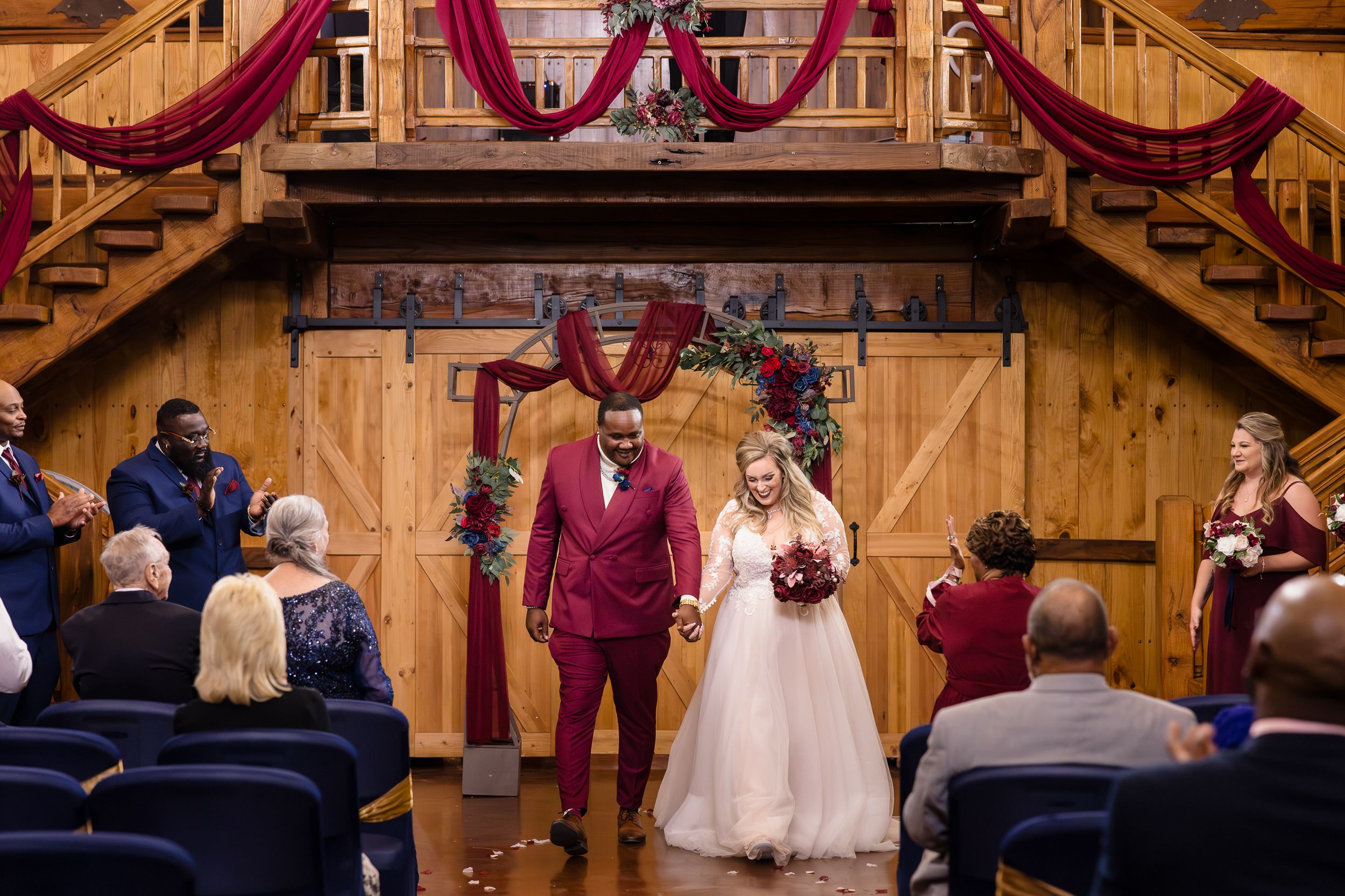 Rustic barn wedding venue decorated with burgundy drapes and wooden beams.