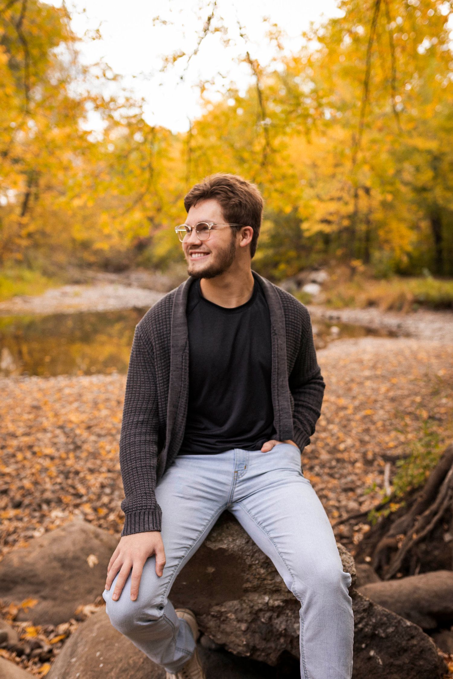 A casual autumn portrait of someone sitting on rocks surrounded by golden fall foliage.