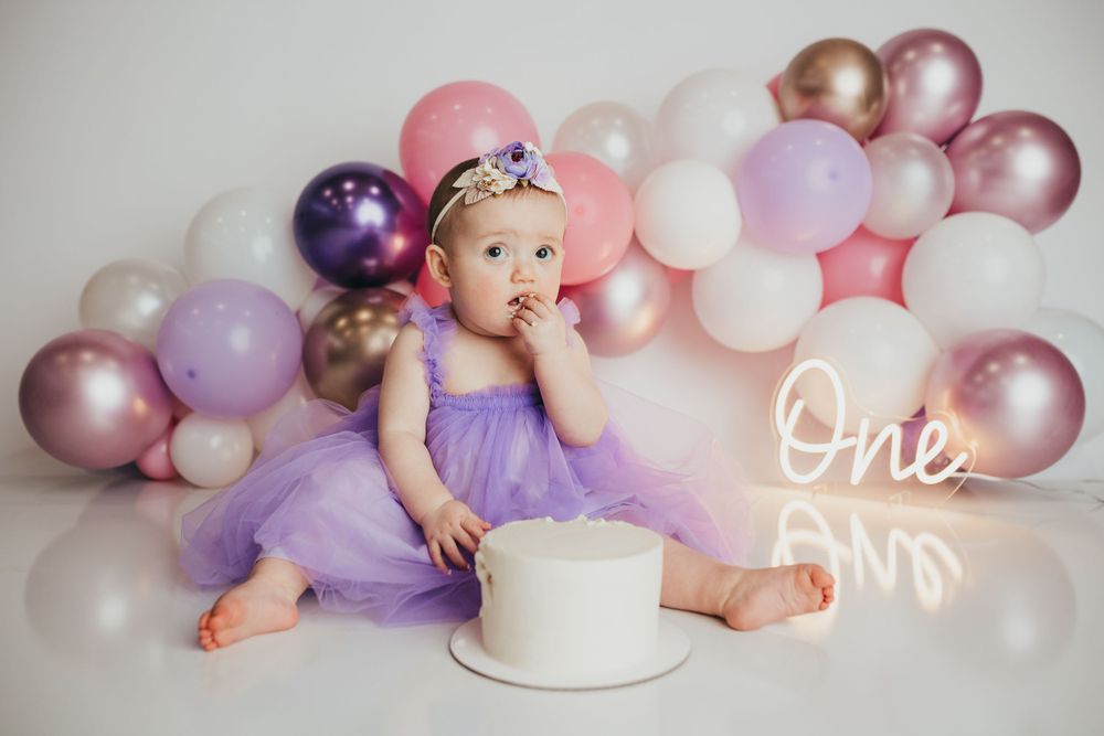 Birthday celebration setup with white cake and balloon arch in pink, purple and rose gold colors.