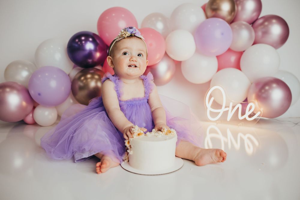 First birthday setup with purple tulle dress, white cake and pink balloon arch backdrop.