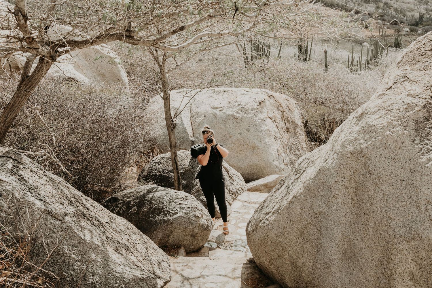 A silhouette of a person standing between large boulders in a mountainous landscape.