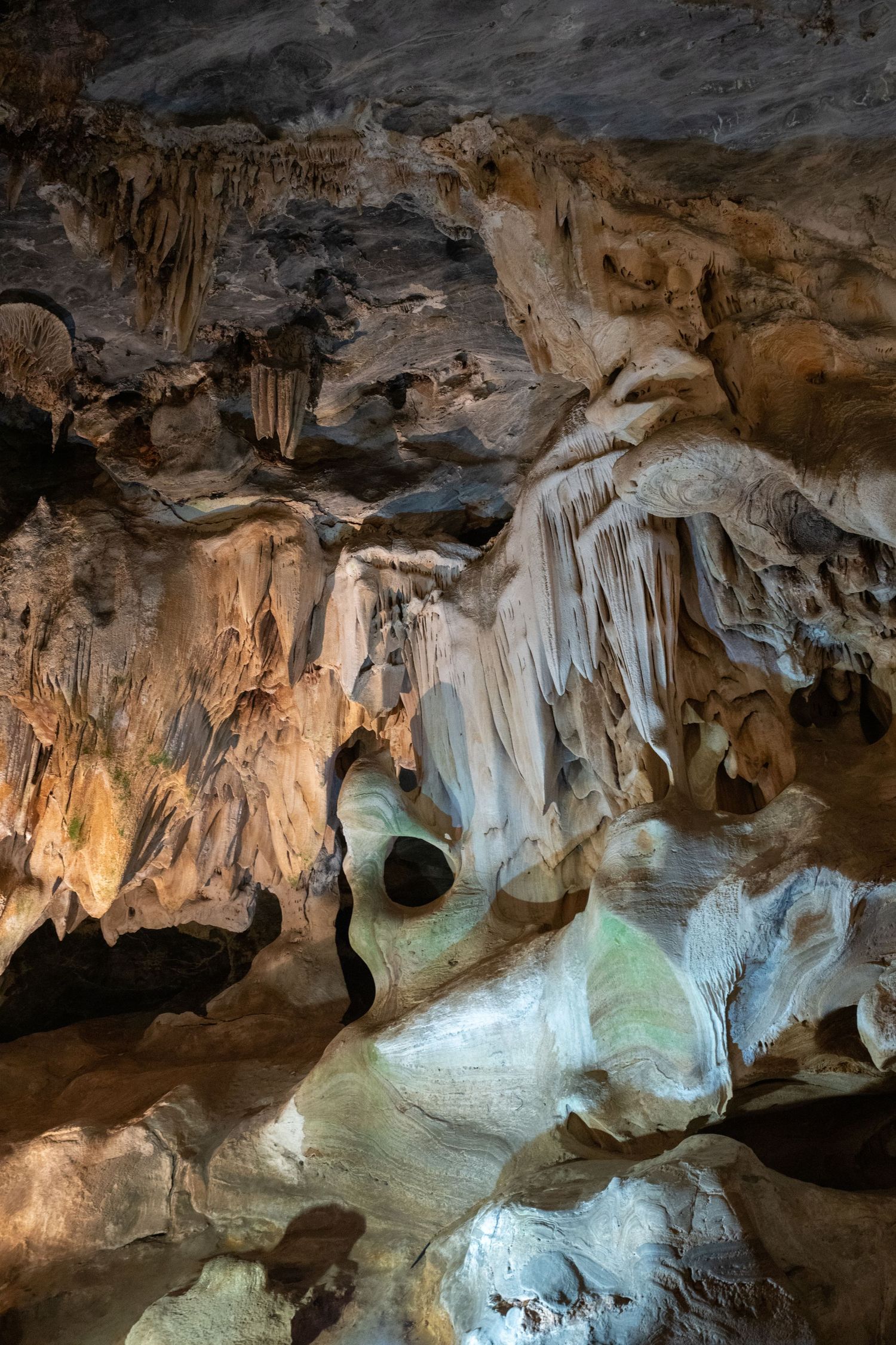 Illuminated limestone cave with dramatic stalactites and rock formations.