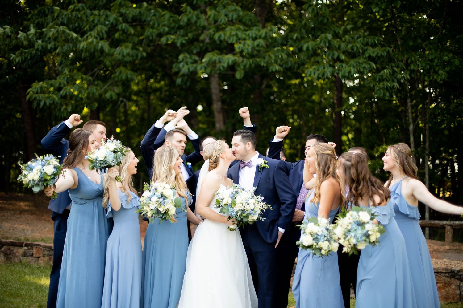 Wedding party in light blue dresses celebrates outdoors in a garden setting.