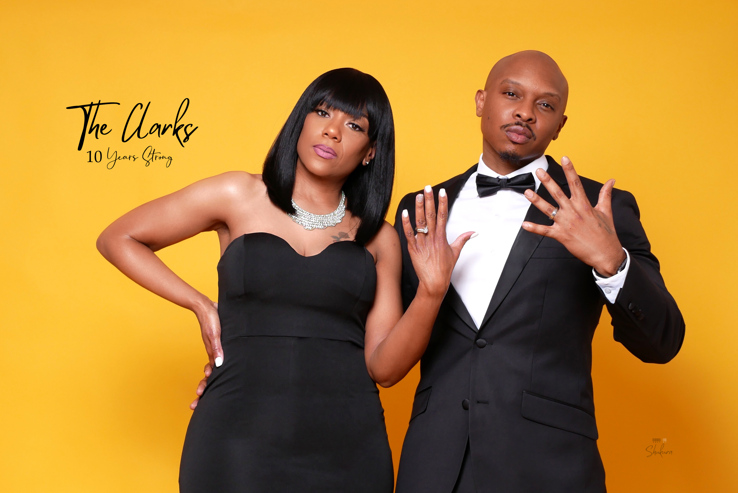 Stylish couple in black formal wear strike a confident pose against vibrant yellow backdrop.
