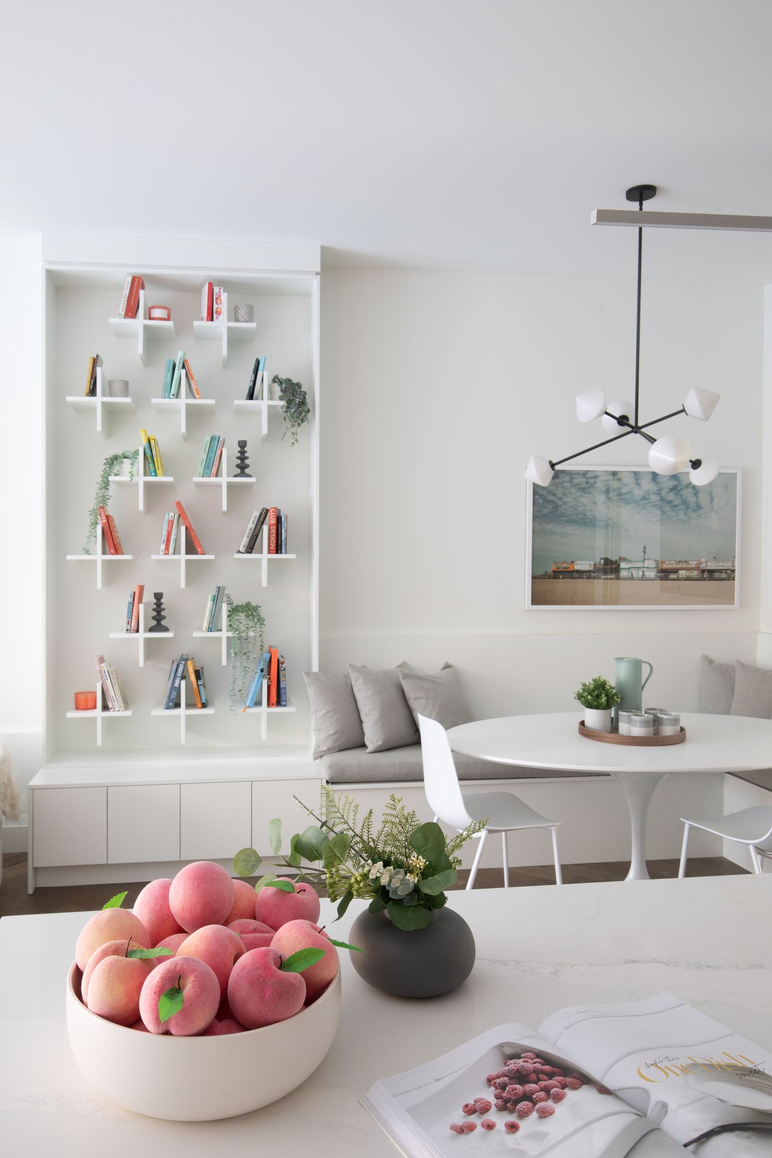Modern dining room with built-in bookshelves, white table, and peaches in a bowl.