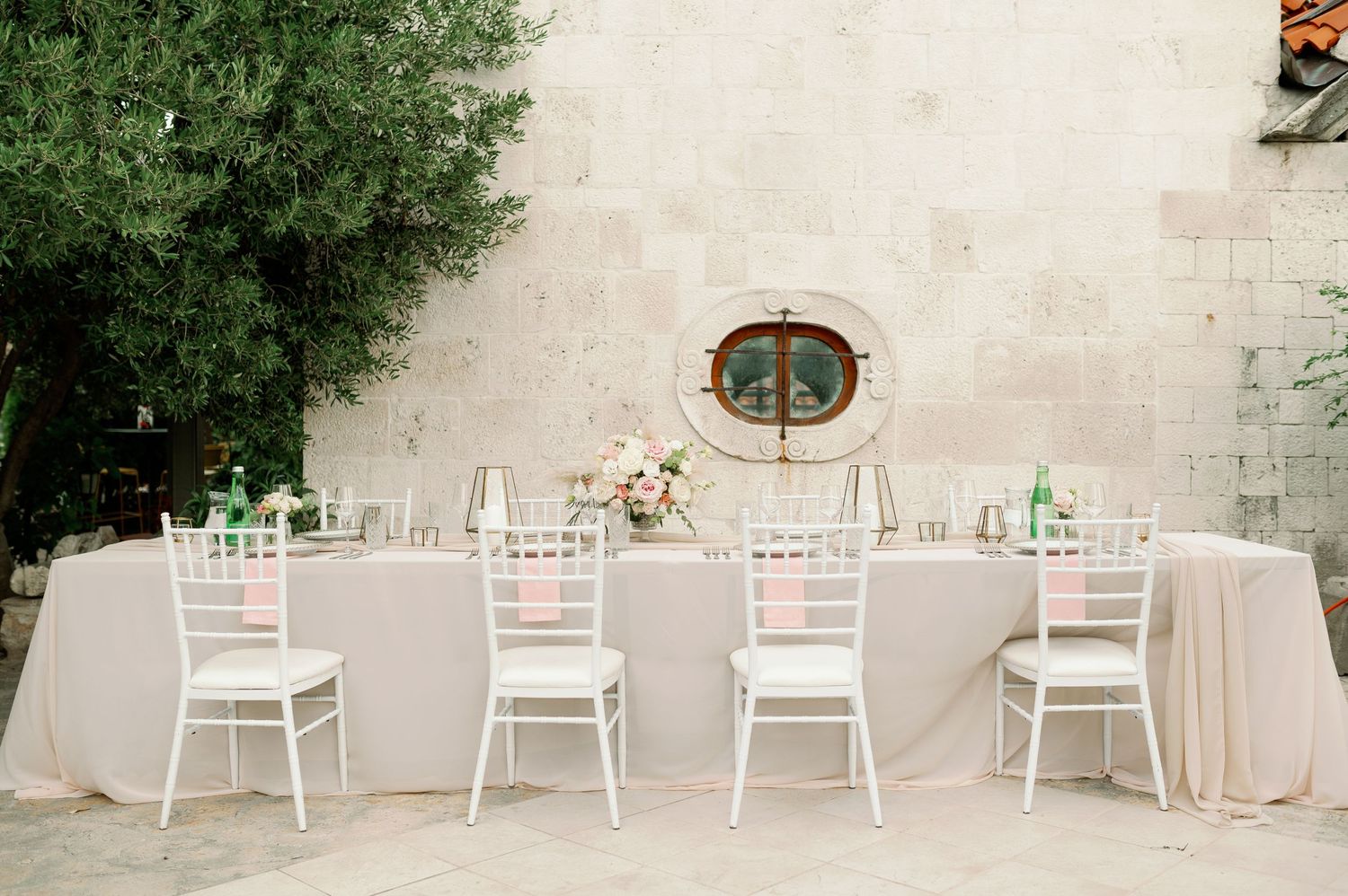 Elegant wedding reception table setup with white chiavari chairs and blush linens.