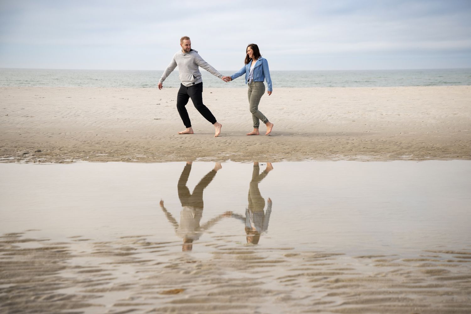 Two people jumping on a beach with their reflections mirrored in wet sand at low tide.