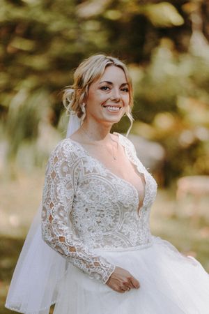 Close up details of bride wearing elegant lace long sleeve wedding gown in natural outdoor setting.