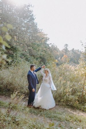 Wedding couple dancing in a sunlit natural setting surrounded by autumn foliage.
