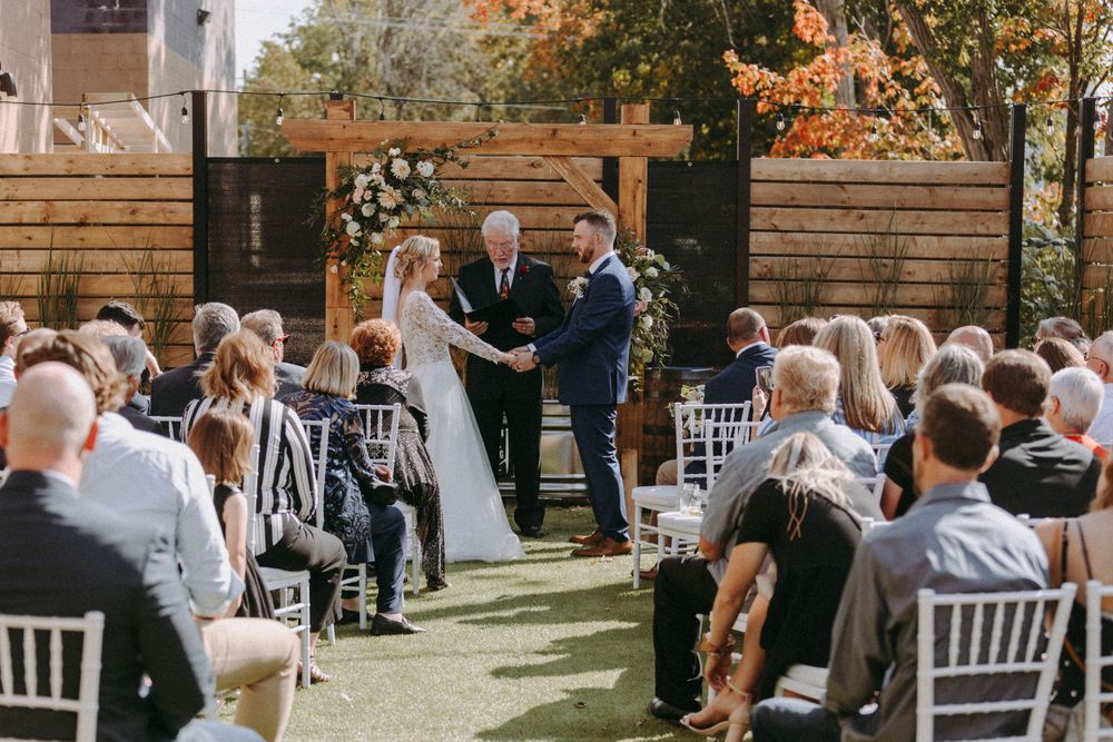 Outdoor wedding ceremony setup with white chairs and wooden fence backdrop in autumn setting.