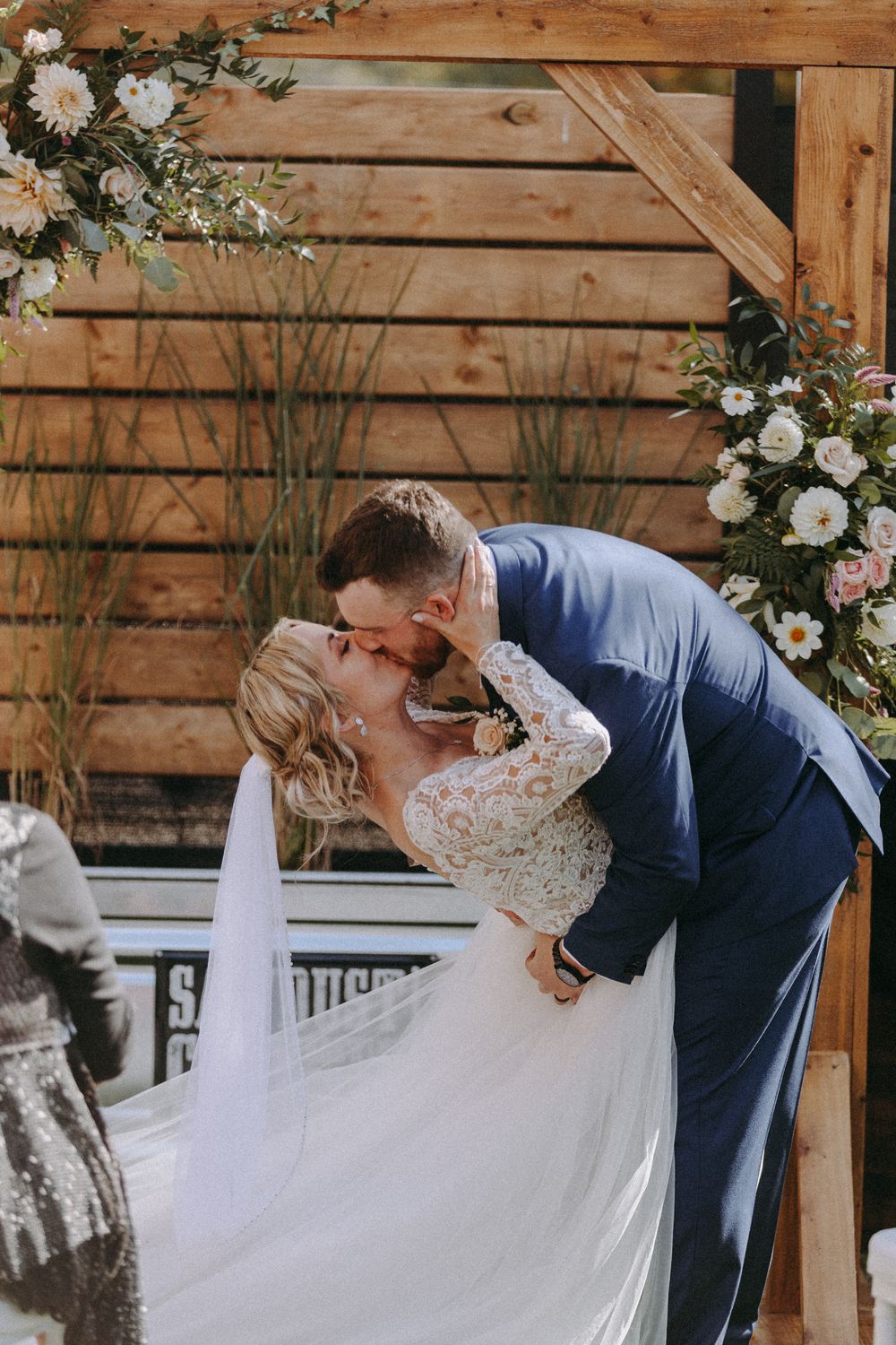 Romantic wedding moment captured against rustic wooden backdrop with floral decorations.