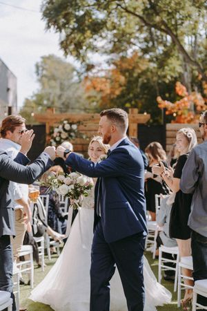 Celebratory moment at outdoor wedding ceremony with guests clapping near wooden fence.