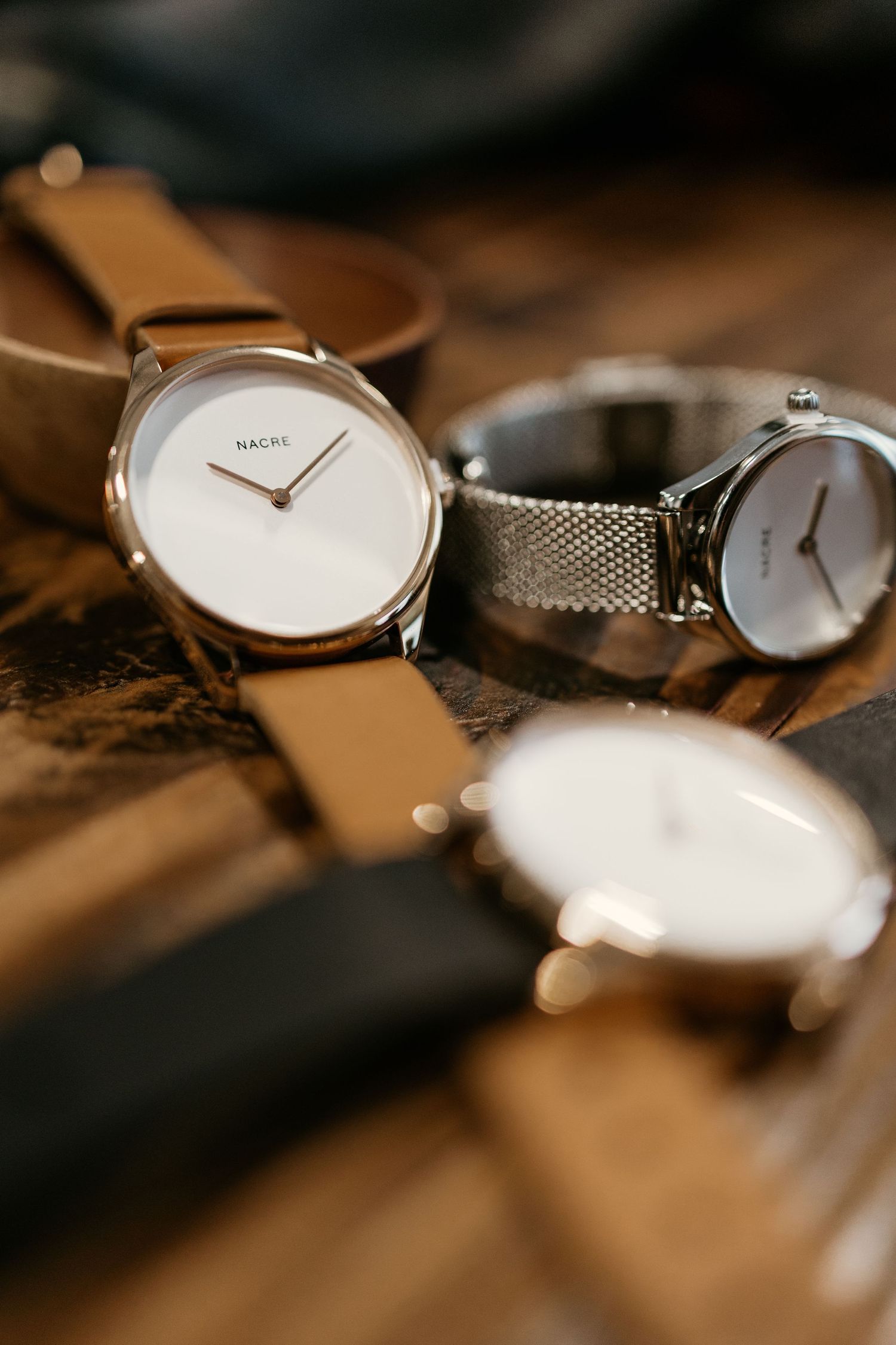 Collection of minimalist watches with mesh and leather straps displayed on wooden background.