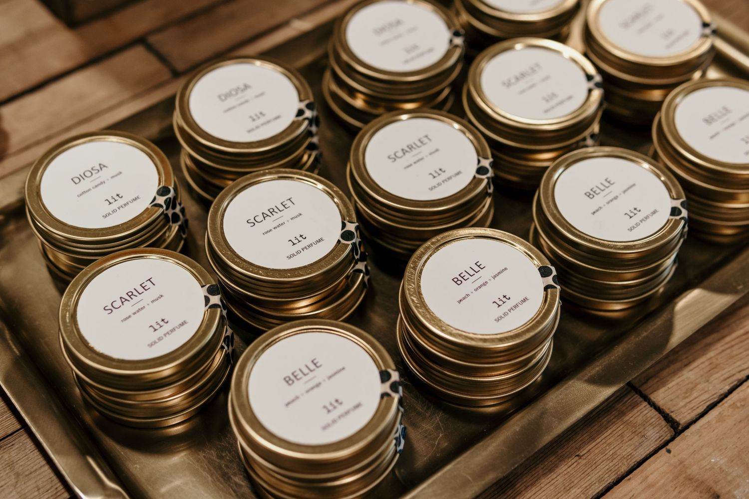 Rows of labeled glass jars with gold lids arranged on wooden surface.