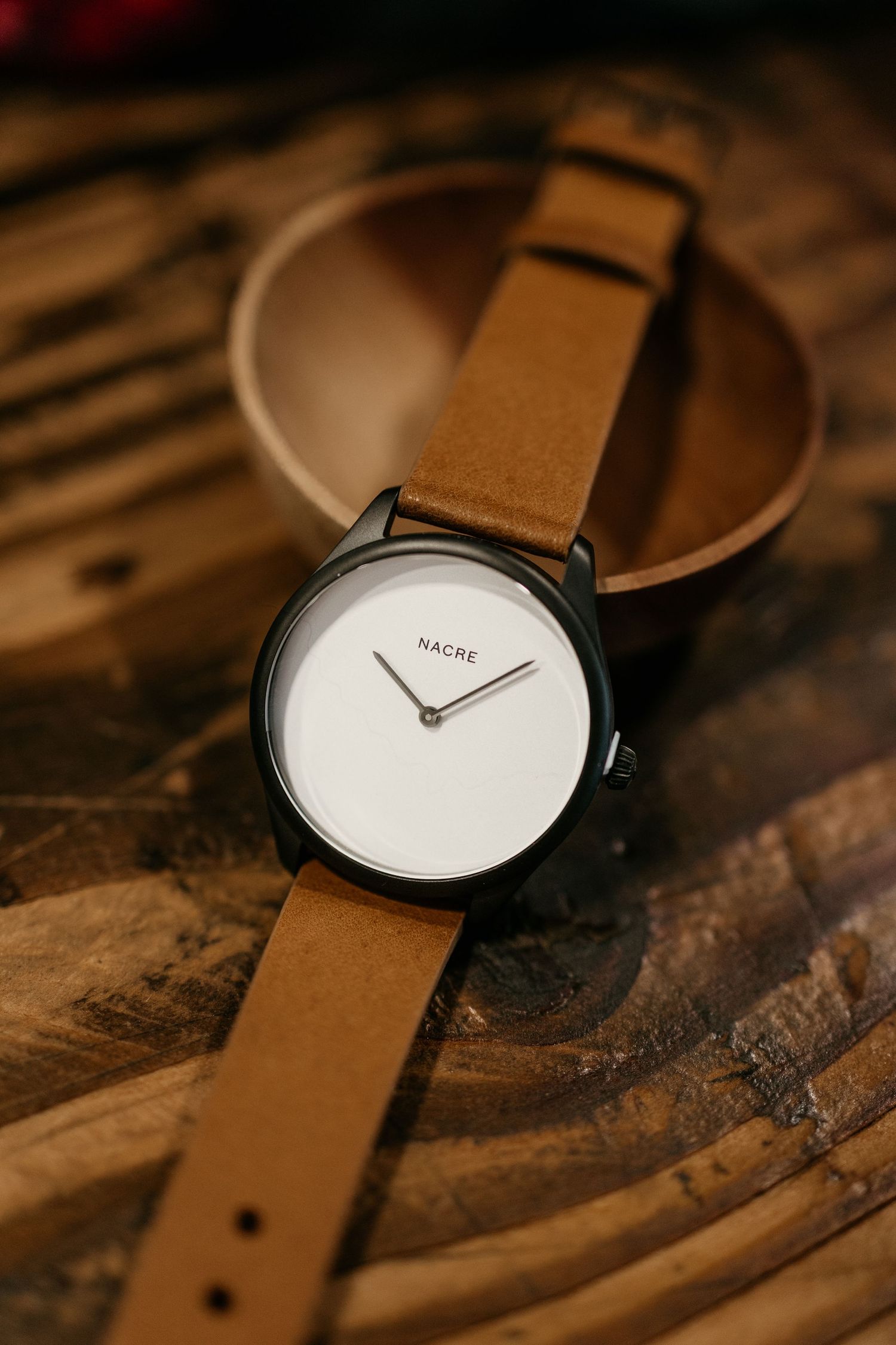 Sleek watch with brown leather strap and white dial photographed on rustic wood.