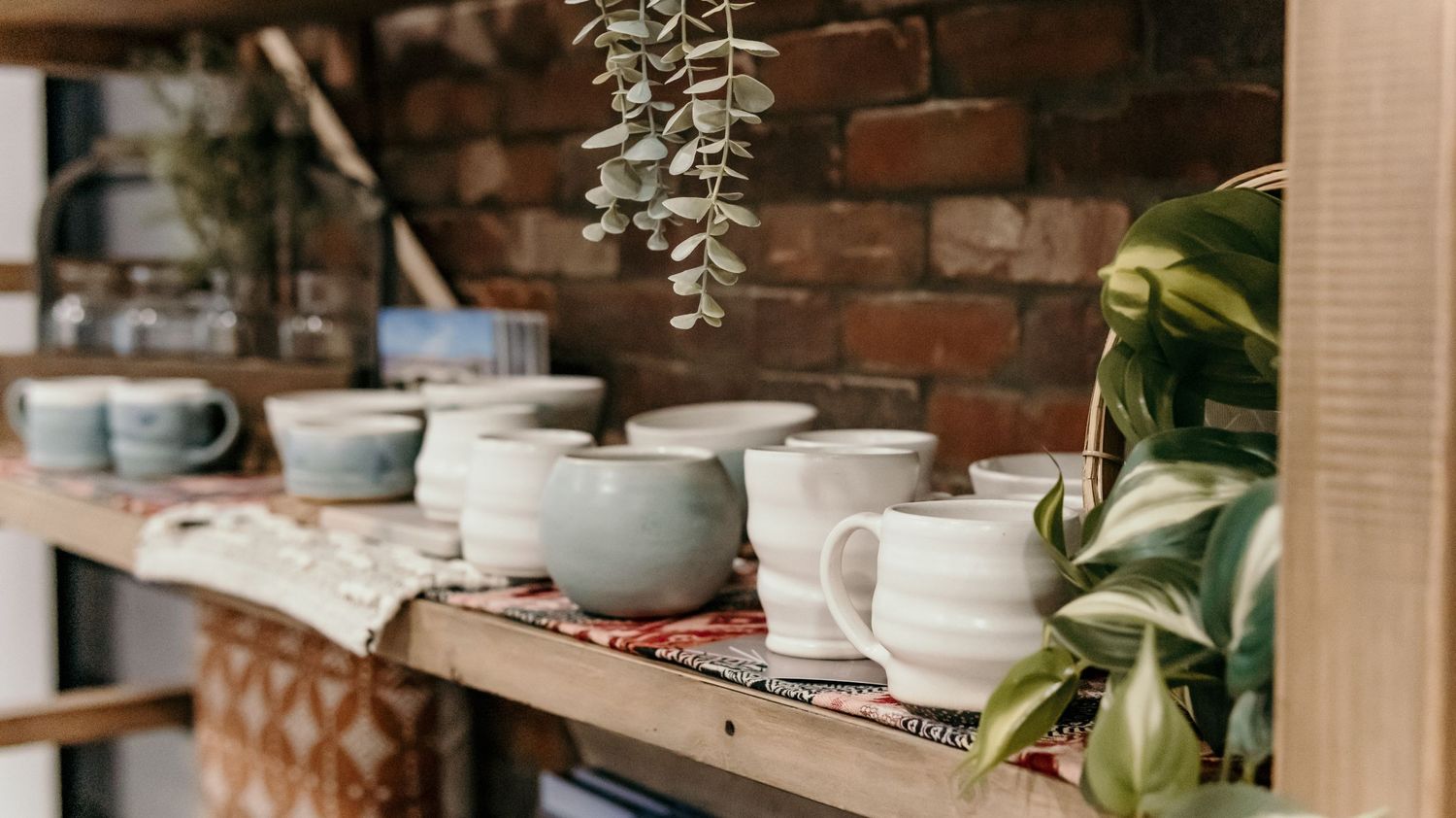Rustic brick wall shelving with potted plants and ceramic decor items.