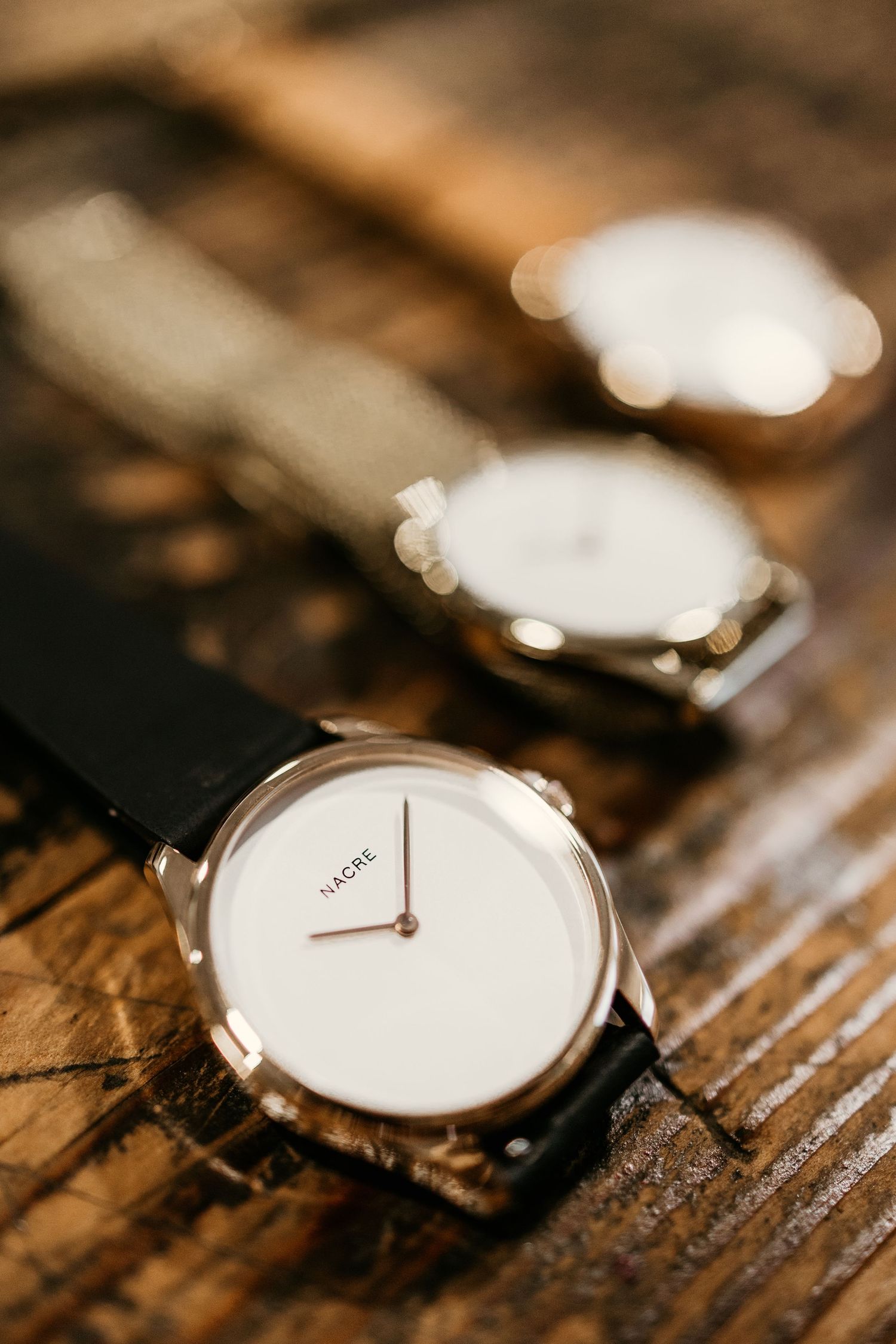 Minimalist white watch face photographed at various angles on rustic wooden surface.